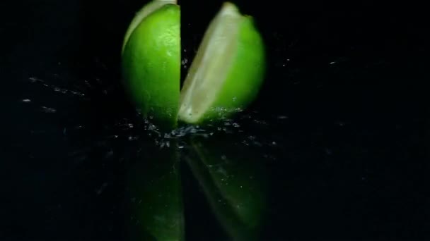 Cuatro pedazos de cal caen sobre la mesa en el agua. Fondo negro. Movimiento lento — Vídeo de stock