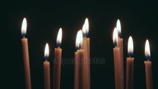 Muchas velas giran en un soporte. Fondo negro — Vídeos de Stock