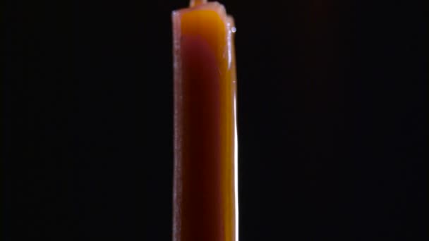 Vosk kape na hořící svíčku. Černé pozadí. Detailní záběr — Stock video