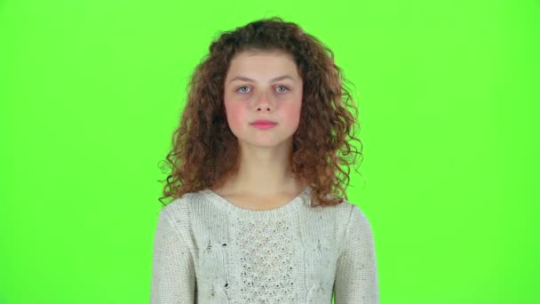Teenage girl smiles and looks into the distance, covering her face with her hands. Green screen — Stock Video