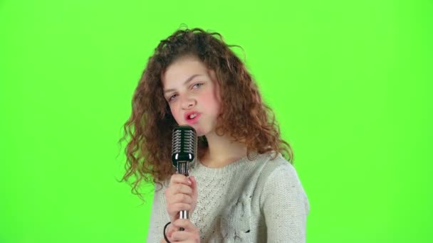 Девочка-подросток поет в огненных песнях ретро-микрофона. Зеленый экран — стоковое видео
