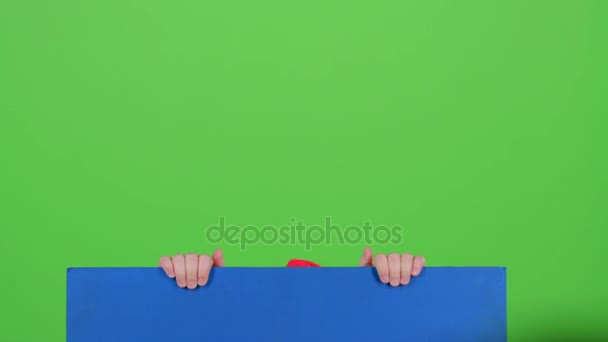 Adolescente en la tapa emerge de detrás del tablero en una pantalla verde — Vídeos de Stock