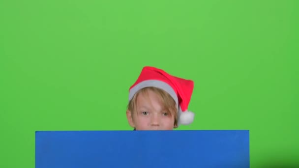 Junge guckt hinter blauem Plakat hervor und winkt mit der Hand vor grünem Bildschirm — Stockvideo