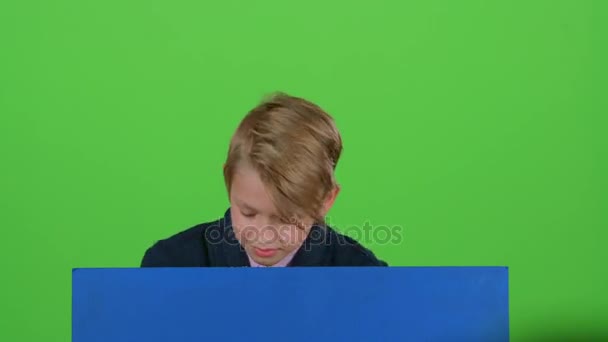 Der Junge, der hinter einem blauen Plakat auftauchte, um ihn anzusehen, scheint sich wieder zu verstecken. Green Screen — Stockvideo