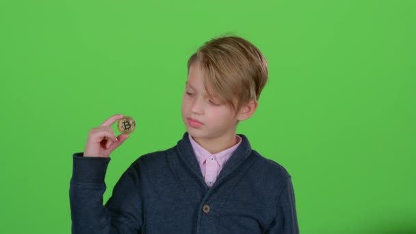 Bambino ragazzo alza la mano e mostra il bitcoin su uno schermo verde — Video Stock