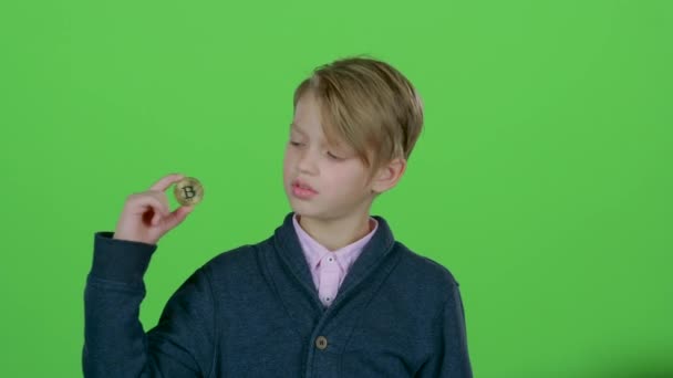Мальчик поднимает руку и показывает золотой биткойн на зеленом экране. — стоковое видео