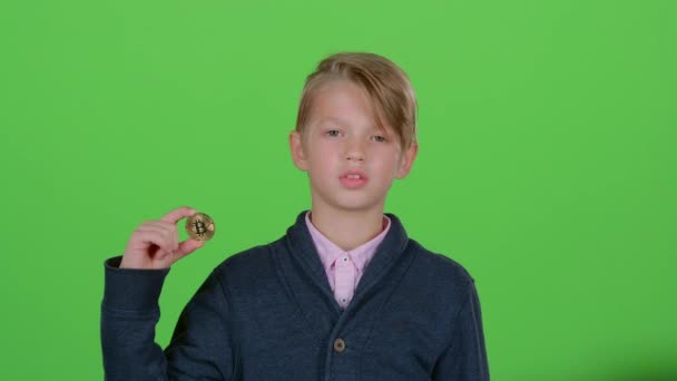 Gyermek fiú felemeli a kezét, és azt mutatja, a gold chip és ellenszenv mutat egy zöld képernyő — Stock videók