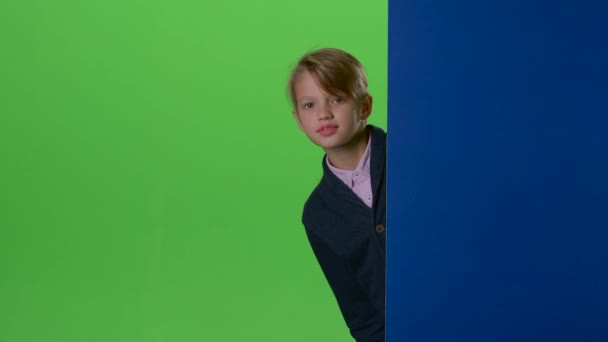 Tiener gluurt uit achter een bord op een groen scherm — Stockvideo