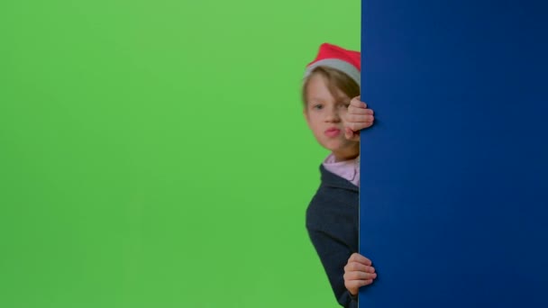 Adolescente en sombrero de Navidad emerge de detrás de las tablas y muestra su puño en una pantalla verde — Vídeos de Stock