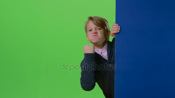 Teenage wyłania się zza deski i pokazuje jego pięść na zielony ekran — Wideo stockowe