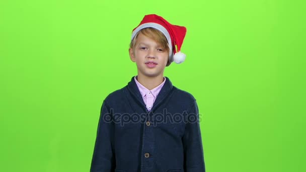 Niño en la tapa de santaclaus levanta la mano y muestra la tarjeta en una pantalla verde. Movimiento lento — Vídeo de stock