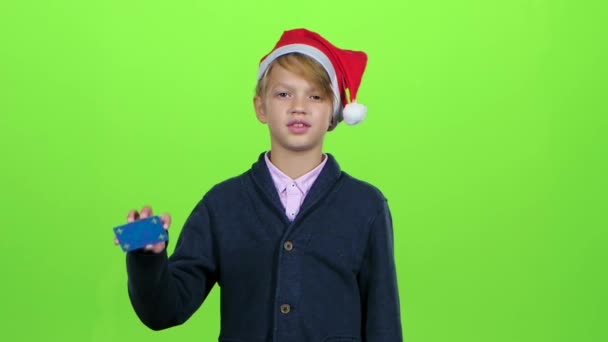 Adolescente en el sombrero de año nuevo con una tarjeta de crédito muestra como en una pantalla verde. Movimiento lento — Vídeo de stock