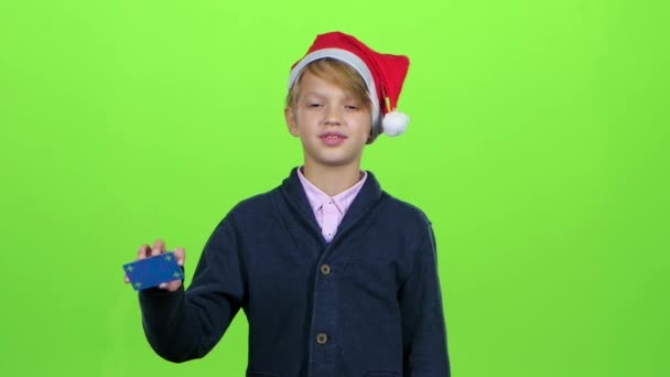 Подросток в новогодней шляпе с кредитной картой показывает неприязнь на зеленом экране. Медленное движение — стоковое видео