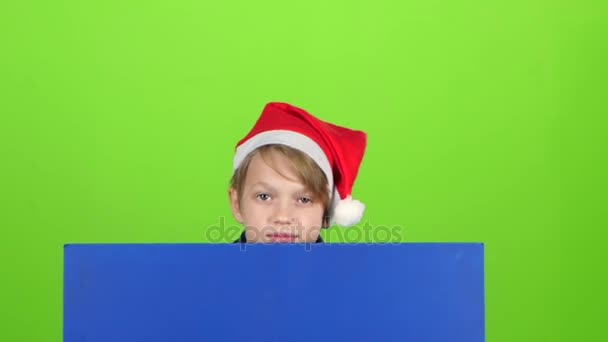 Adolescente en un sombrero rojo aparece de un tablero en una pantalla verde. Movimiento lento — Vídeo de stock