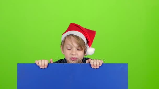 Glad liten pojke som kikar ut från bakom affischen stiger håller för en skylt på en grön skärm. Slow motion — Stockvideo