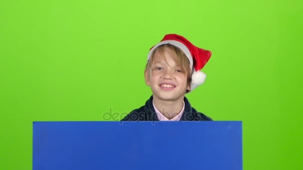 Ребенок, выглядывающий из-за синего плаката, машет рукой перед зеленым экраном. Медленное движение — стоковое видео