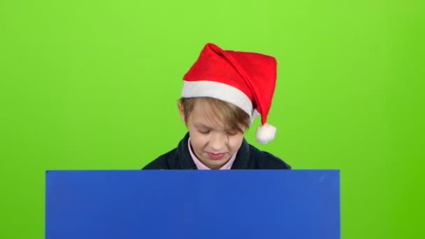 Barn pojke dök upp bakom en blå affisch att titta på honom skakar på huvudet och döljer igen. Grön skärm. Slow motion — Stockvideo