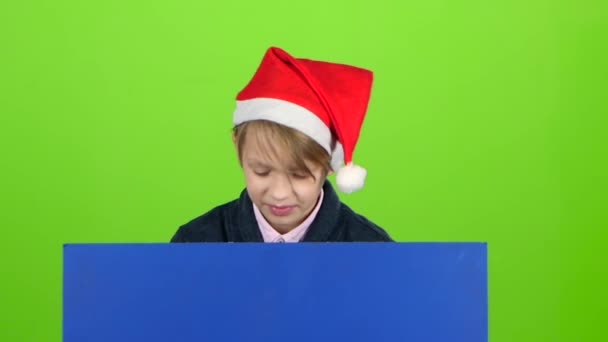 Niño más joven apareció detrás de un cartel azul apunta a sus dedos índice. Pantalla verde. Movimiento lento — Vídeos de Stock