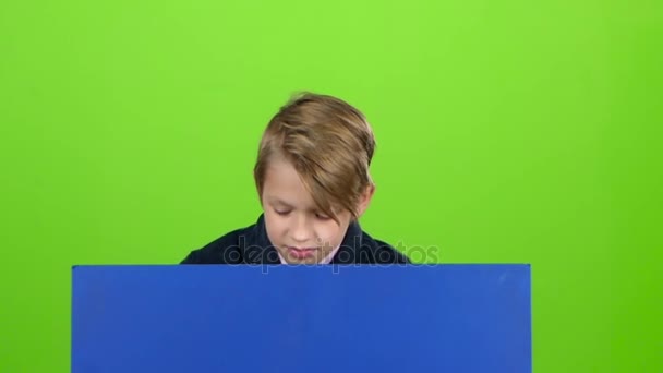 Der Junge, der hinter einem blauen Plakat auftauchte, um ihn anzusehen, scheint sich wieder zu verstecken. Green Screen. Zeitlupe — Stockvideo