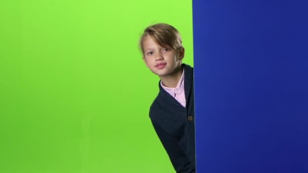 Έφηβο κρυφοκοιτάζει έξω από πίσω από έναν πίνακα σε μια πράσινη οθόνη. Αργή κίνηση — Αρχείο Βίντεο
