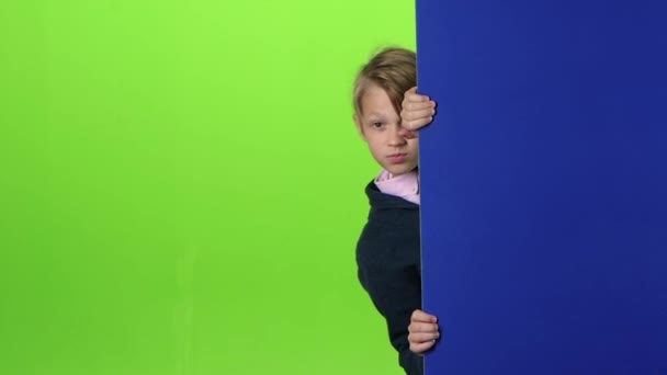 Teenager im Pullover lugt hinter den Brettern hervor und zeigt sich wie auf einem grünen Bildschirm. Zeitlupe — Stockvideo
