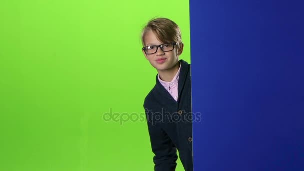 Счастливый мальчик в очках выглядывает из стены на зеленый экран. Медленное движение — стоковое видео