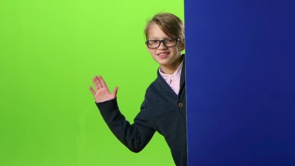 Chłopiec dziecko w okularach ćwierkania na zewnątrz od ściany niebieskie na zielonym ekranie. Zwolnionym tempie — Wideo stockowe
