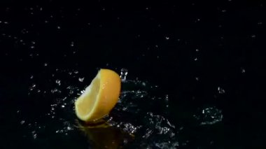 Portakal dilim suya düşüyor. Siyah arka plan. Ağır çekim