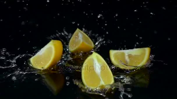 Πορτοκαλί πέφτει στο νερό και διαλείμματα μέχρι σε τέσσερα μέρη. Μαύρο φόντο. Αργή κίνηση — Αρχείο Βίντεο