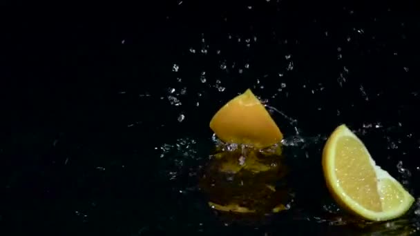 Πορτοκαλί πέφτει στο νερό και διαλείμματα επάνω σε δύο μέρη. Μαύρο φόντο. Αργή κίνηση — Αρχείο Βίντεο
