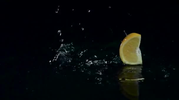 Une tranche d'orange tombe dans l'eau. Fond noir. Mouvement lent — Video