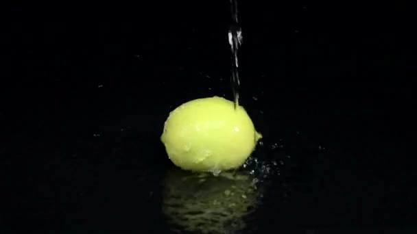 Лимон в воде, капли чистой воды льют на него сверху. Чёрный фон. Медленное движение — стоковое видео