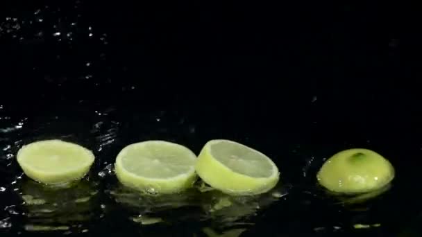 O limão dissolve-se em fatias quando cai na água. Fundo preto. Movimento lento — Vídeo de Stock