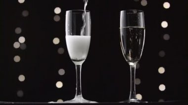 İki şeffaf cam içine dökülür varlık şampanya. Bokeh arka plan siyah yanıp sönen