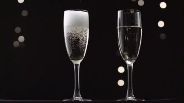 Soğuk şampanya şişe iki şeffaf cam içine dökülür. Bokeh arka plan siyah yanıp sönen
