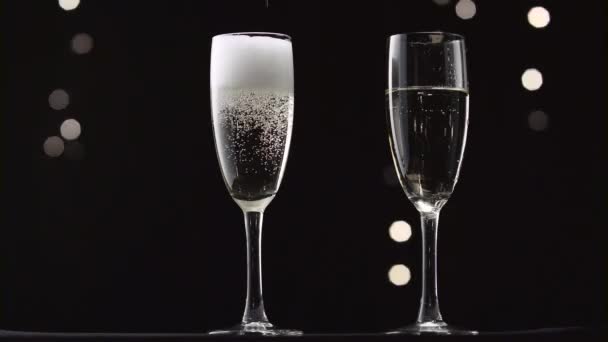 Champagne froid versé dans deux verres transparents de la bouteille. Bokeh clignotant fond noir — Video