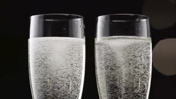 Two flutes of chilled sparkling wine. Bokeh blinking black background. Close up — Stock Video