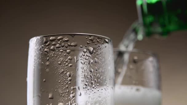 Mousserende wijn stroomt uit een groene fles in twee stomende glas. Close-up — Stockvideo