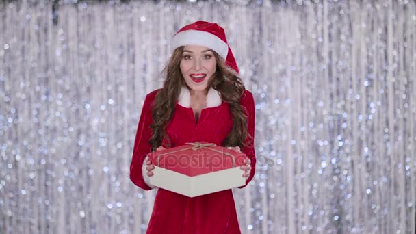 Santa flicka innehar en gåva i händerna och visar ett finger ok. Bokeh bakgrund — Stockvideo