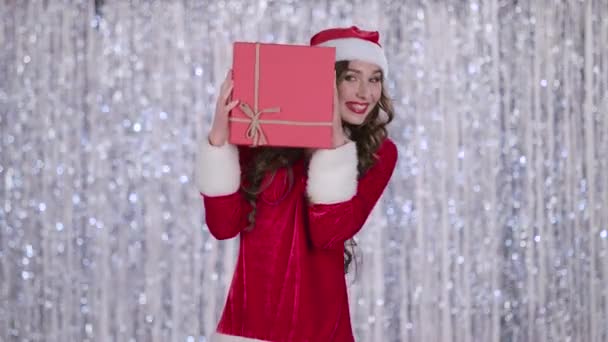 Mädchen im Schneemädchenkostüm hält ein Geschenk in der Hand und winkt, hallo. Bokeh-Hintergrund — Stockvideo