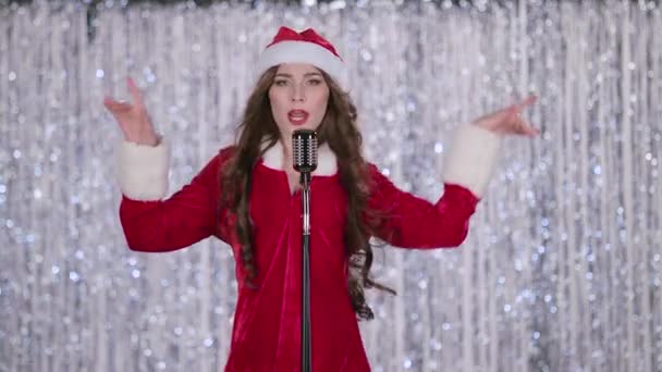 Santa mujer canta en un micrófono retro y baila con música enérgica. Fondo Bokeh. Movimiento lento — Vídeos de Stock