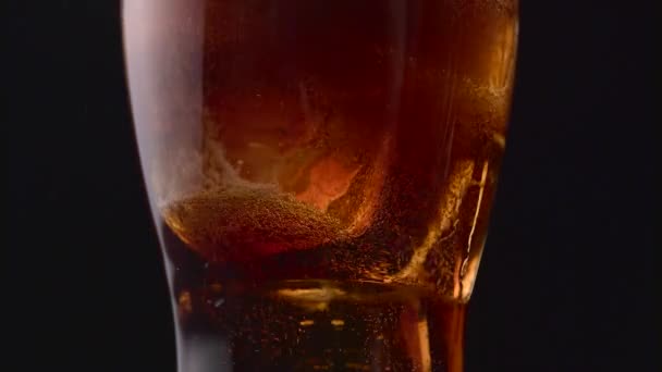 Glass of cola with white bubbles at the bottom. Black background. Close up — Stock Video