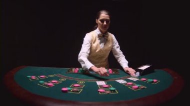 Casino satıcı kartları kart tutucusunu çeker, cips bir poker masasında bırakır. Siyah arka plan. Ağır çekim