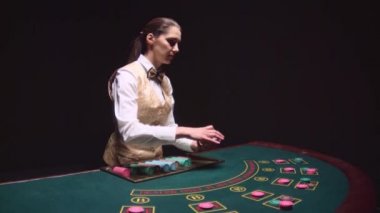 Kumarhane krupiye kız poker masa üstü kartları dağıtır. Siyah arka plan. Ağır çekim