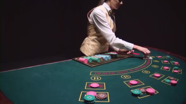 Kaszinó, krupié lány osztja el a kártyát a póker asztallap segítségével vágott kártyát. Fekete háttér. Lassú mozgás — Stock videók