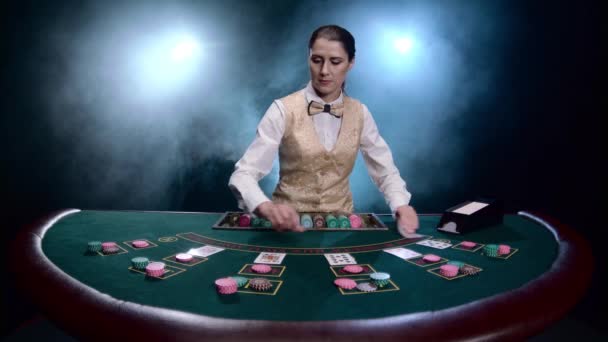 Croupier reparte las cartas desde el titular de la tarjeta sobre fondo ahumado negro con focos. Movimiento lento — Vídeo de stock