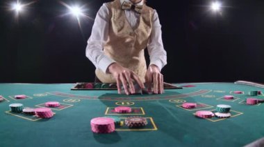 Kumarhane krupiye kesim kartı kullanarak poker masa üstü kartları dağıtır. Siyah arka plan. Parlak ışık. Ağır çekim