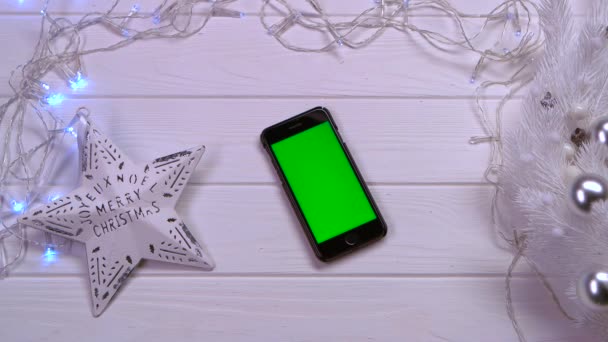 Mobiltelefon fekszik egy fehér asztal, karácsonyi játékok és a koszorúkat. Szemközti nézet — Stock videók