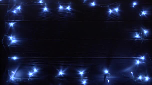 Guirnalda de Navidad quema la luz brillante acostado en una mesa en una habitación oscura. Vista superior — Vídeos de Stock