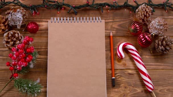 Mockup Cuaderno y lápiz yacen sobre la mesa, juguetes de Navidad y guirnaldas alrededor. Vista superior — Vídeo de stock